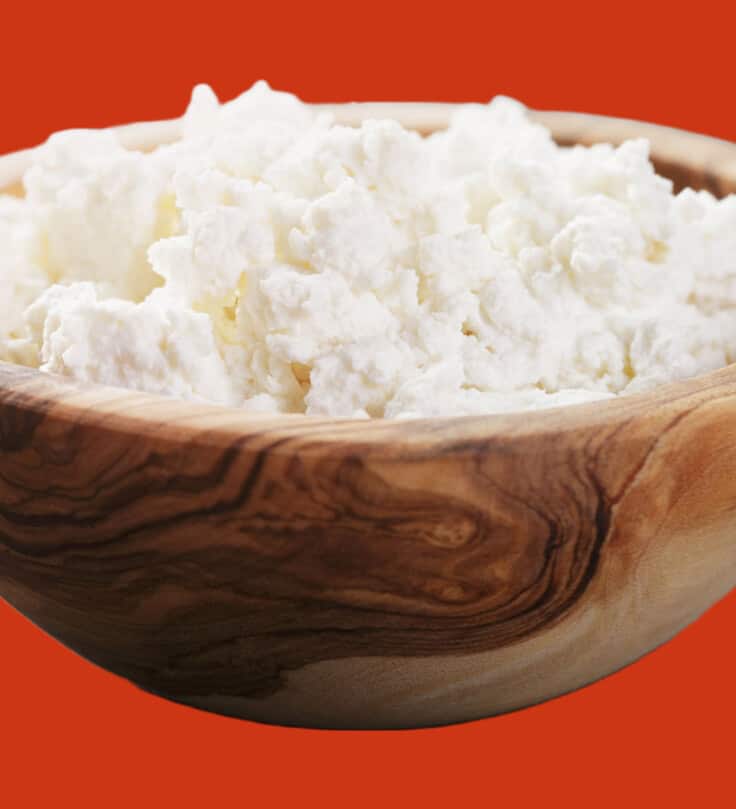 wooden bowl filled with ricotta cheese set on an orange background