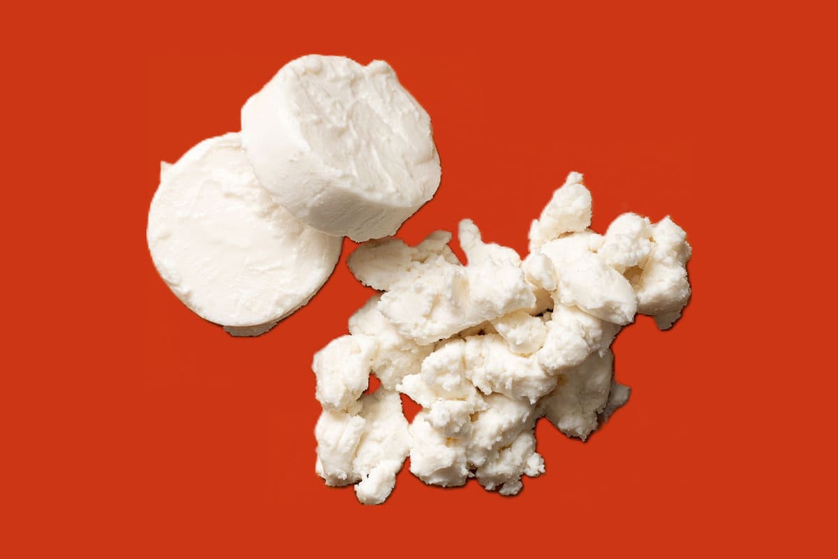 slices of fresh goat cheese and crumbles of fresh goat cheese set on an orange background