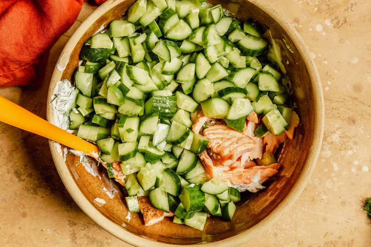 salmon and cucumber chunks in a large brown bowl with a spatula