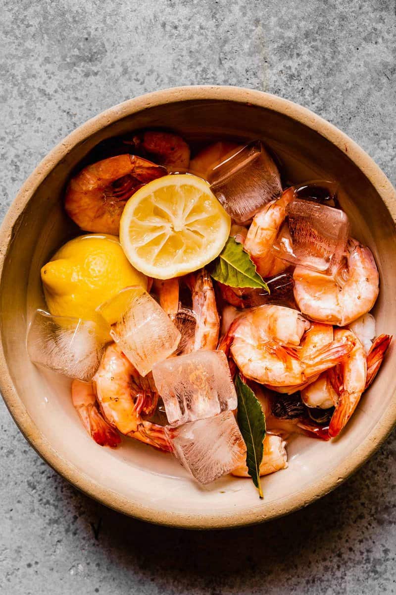 poached shrimp in a large bowl with ice, lemon halves and bay leaves