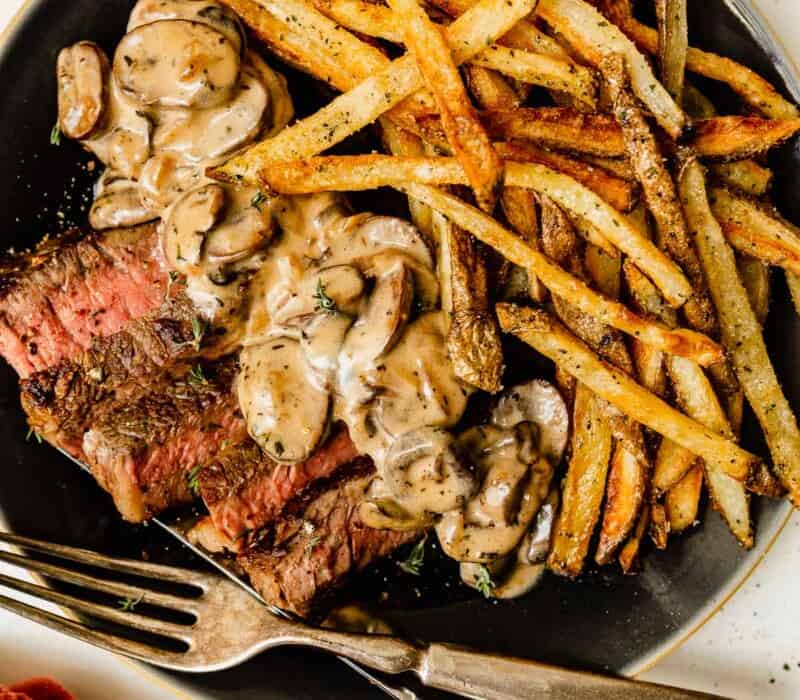 steak frites on a plate with a creamy mushroom sauce.