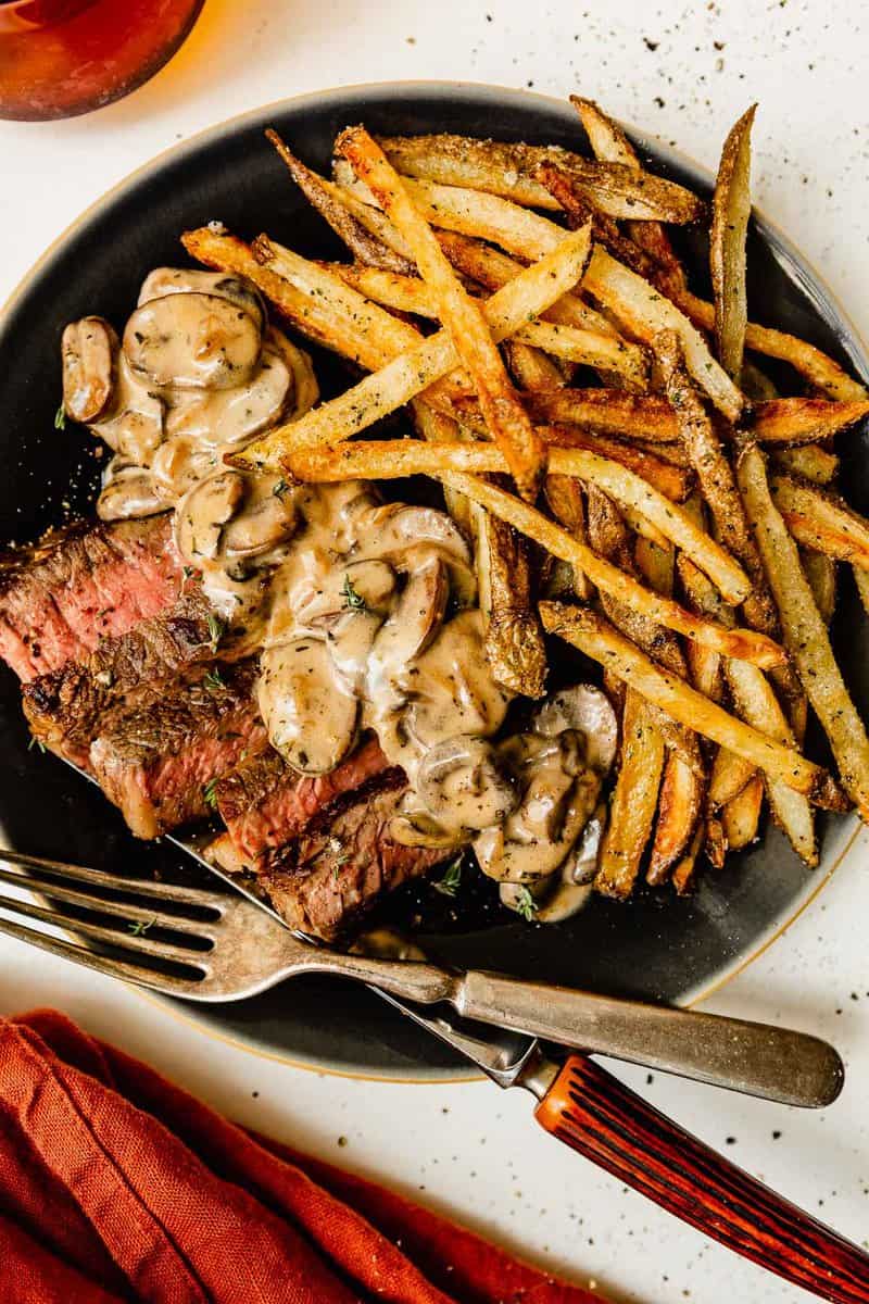 steak frites on a plate with a creamy mushroom sauce.