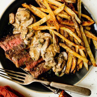 steak and frites on a plate with a creamy mushroom sauce