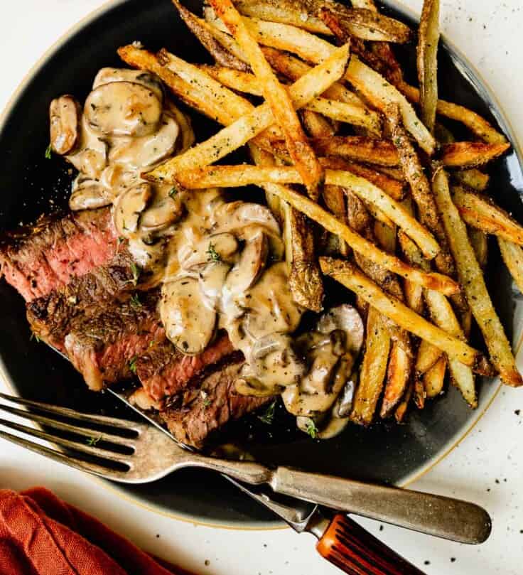 steak and frites on a plate with a creamy mushroom sauce