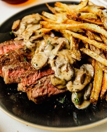 creamy mushroom sauce on top of sliced medium rare steak on a plate with fries