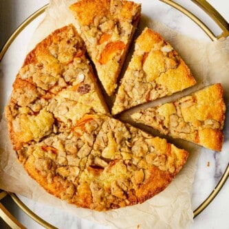 cake with apricots and streusel on top set on a round marble platter lined with parchment paper