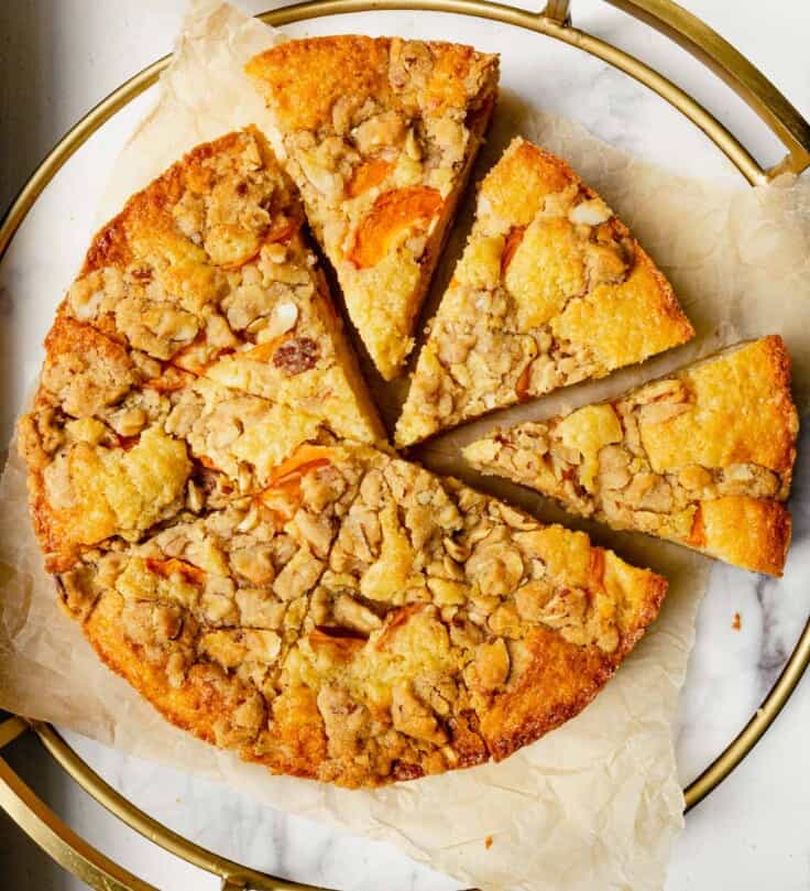 cake with apricots and streusel on top set on a round marble platter lined with parchment paper