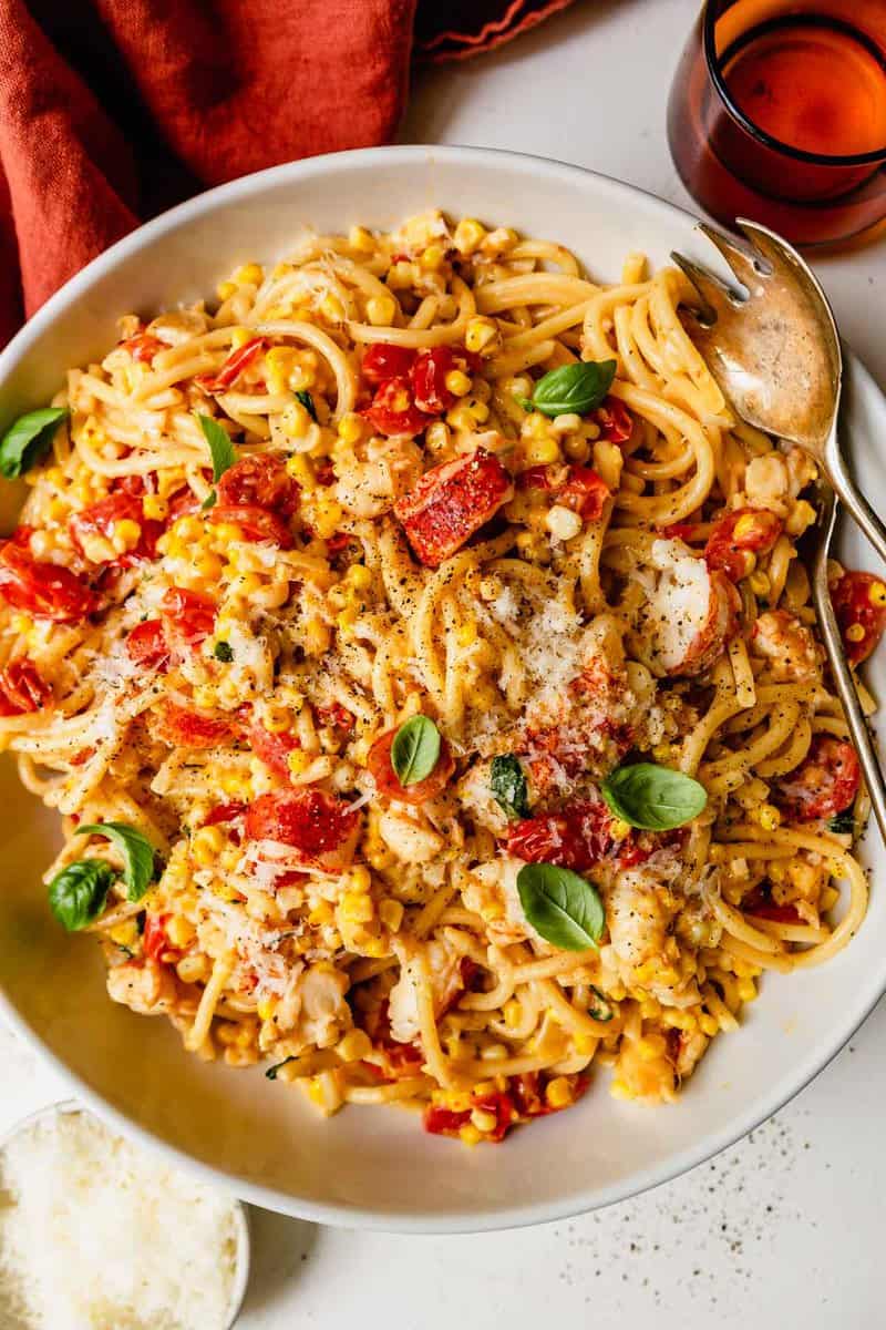 large bowl of pasta with chunks of lobster meat, tomatoes, basil and sweet corn