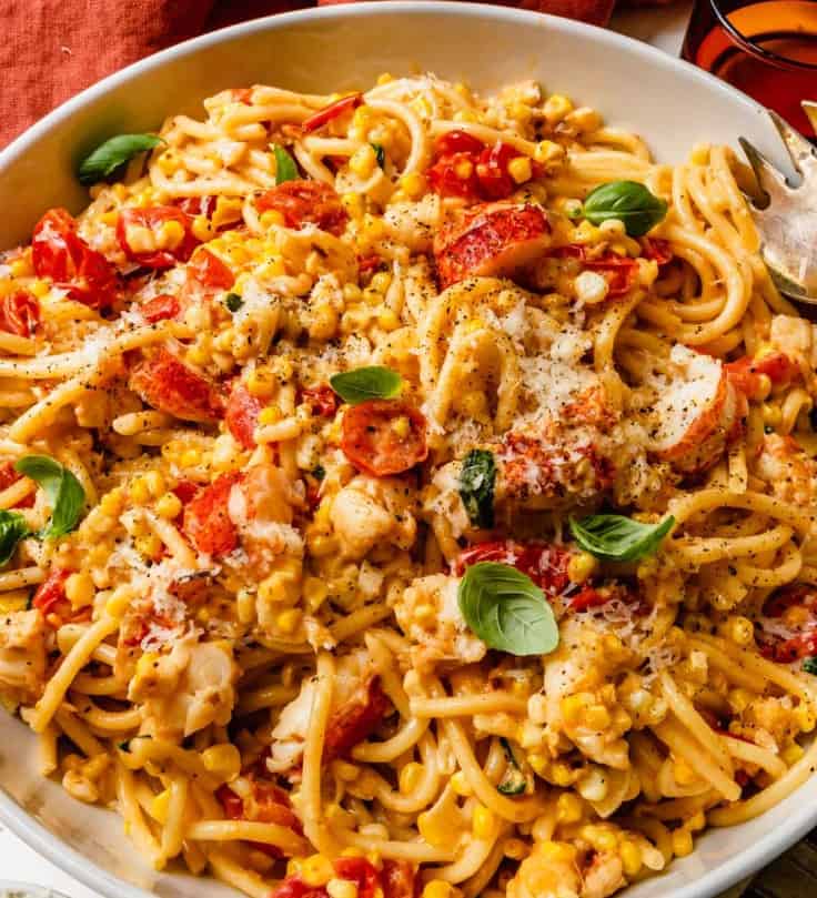 large bowl of pasta with chunks of lobster meat, tomatoes, basil and sweet corn