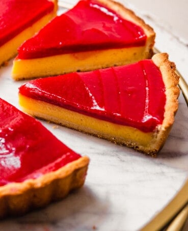 Slices of tart set on a marble tray. Tart slices featuring a layer of lemon curd topped with a layer of red raspberry puree