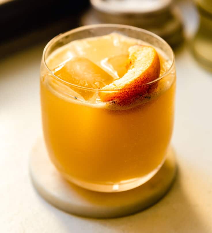 peach cocktail in a rocks glass set on a white counter