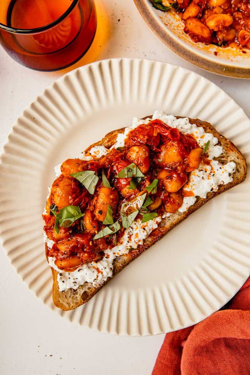 butter beans in a tomato sauce piled onto a piece of toast topped with cottage cheese