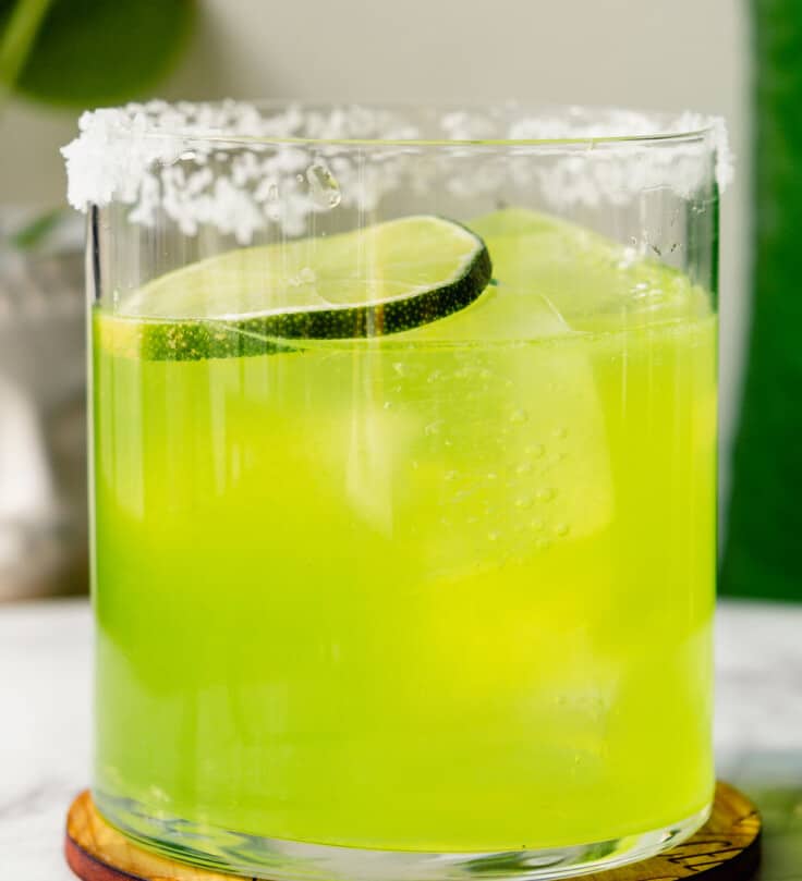 Vibrant green cocktail in a rocks glass rimmed wit salt and garnished with a lime wheel