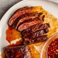 sliced steak on a plate with red sauce brushed over steak and in a bowl set next to steak