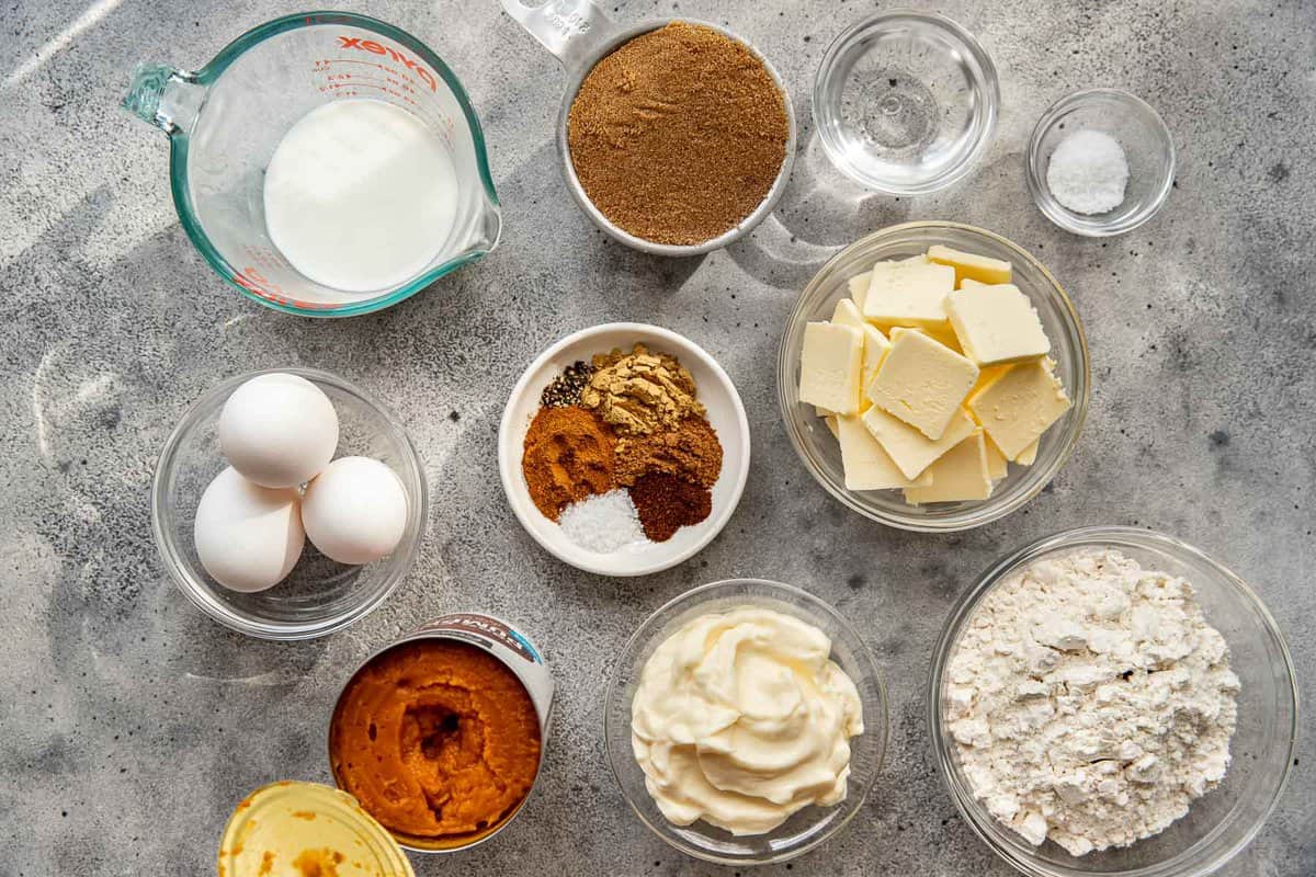 eggs, butter, milk, sugar, flour, pumpkin, mayo, and spices measured out and set on a counter.