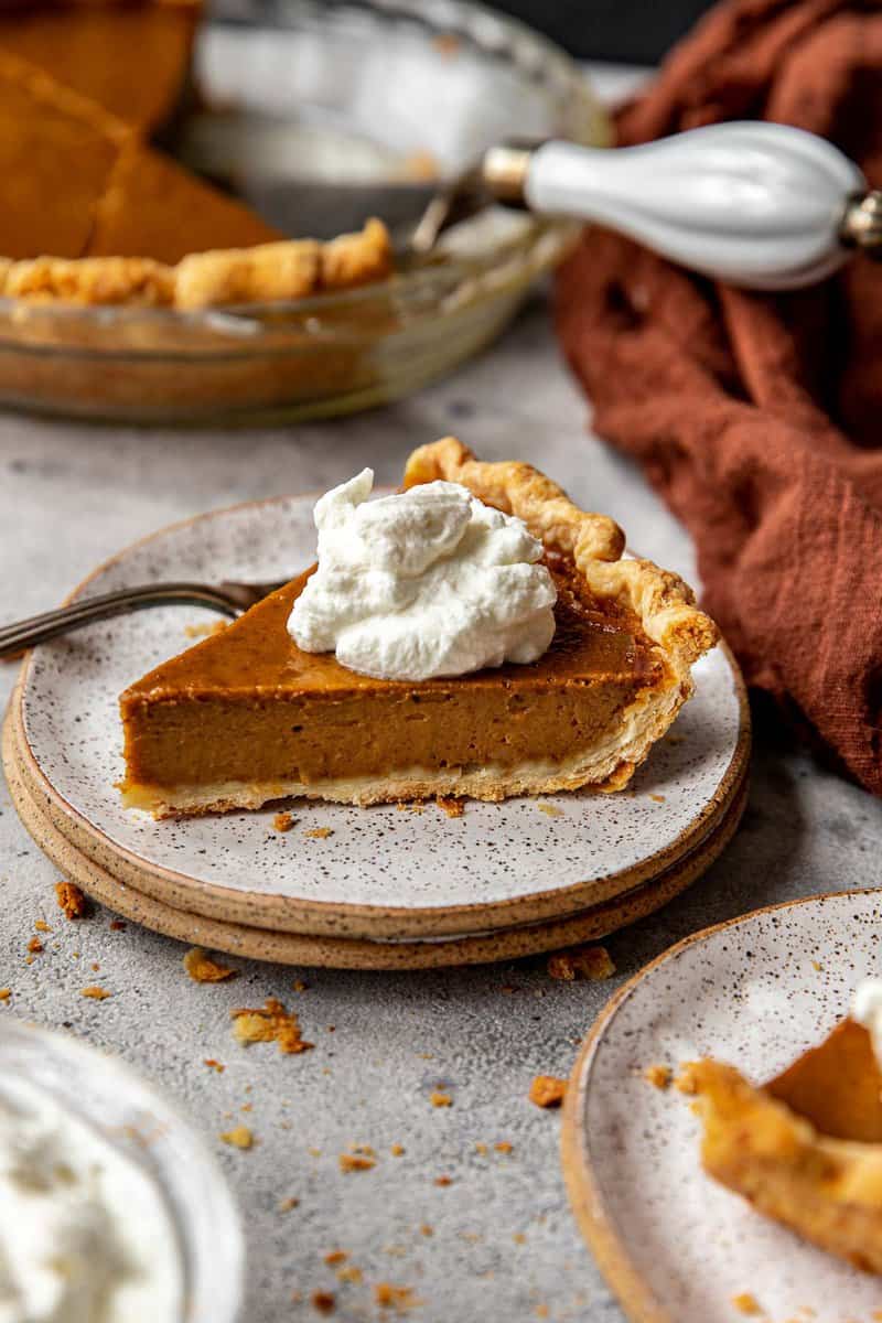 slice of pumpkin pie on a speckled plate with a fork and topped with whipped cream.