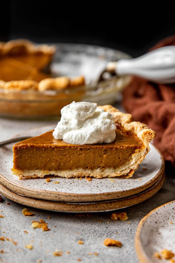 slice of pumpkin pie on a speckled plate with a fork and topped with whipped cream.