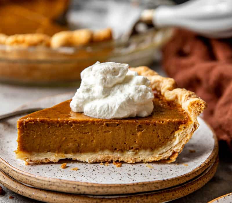 slice of pumpkin pie on a speckled plate with a fork and topped with whipped cream.