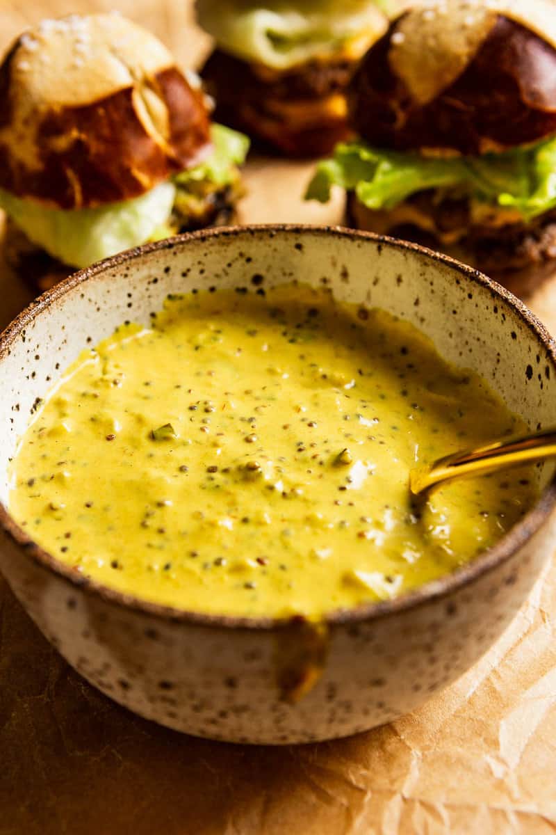 vibrant yellow smash burger sauce in a speckled pottery bowl with a gold spoon set in it