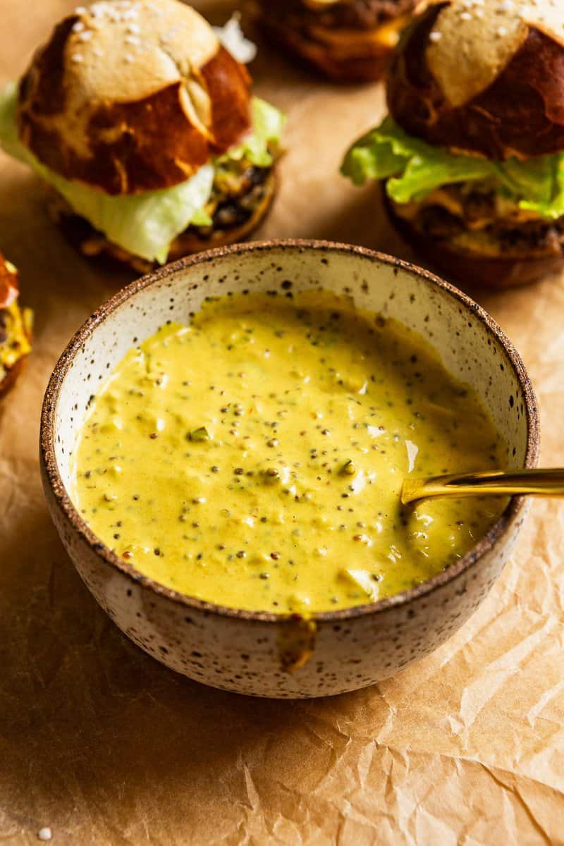 vibrant yellow smash burger sauce in a speckled pottery bowl with a gold spoon set in it