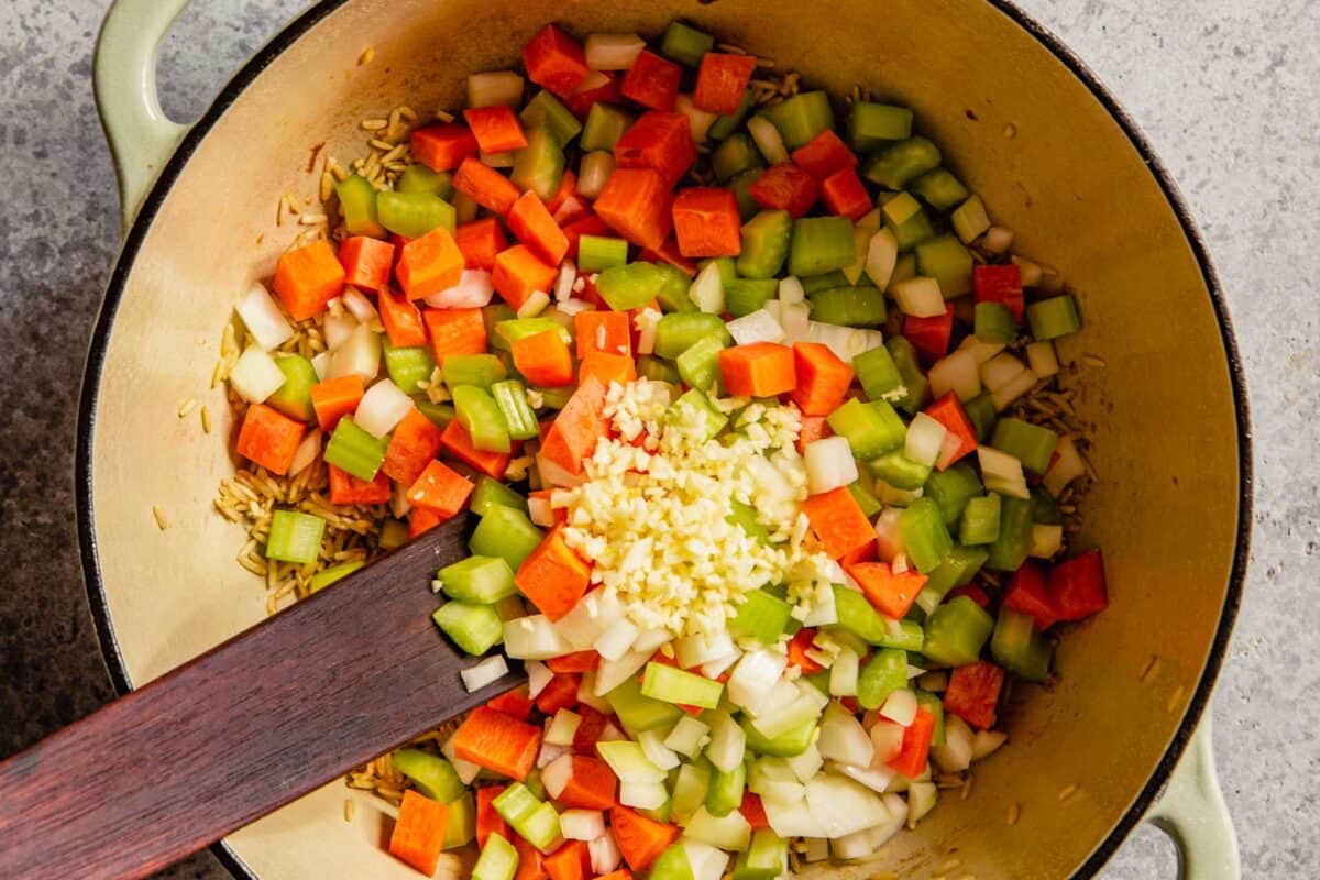 Diced carrots, onion, celery and garlic in a large pot being cooked for chicken rice soup.