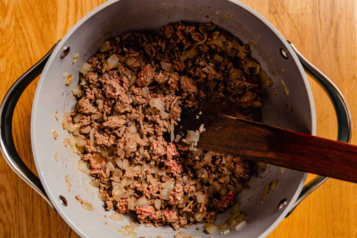 Ground beef cooking in a large gray pot with a wooden spoon.