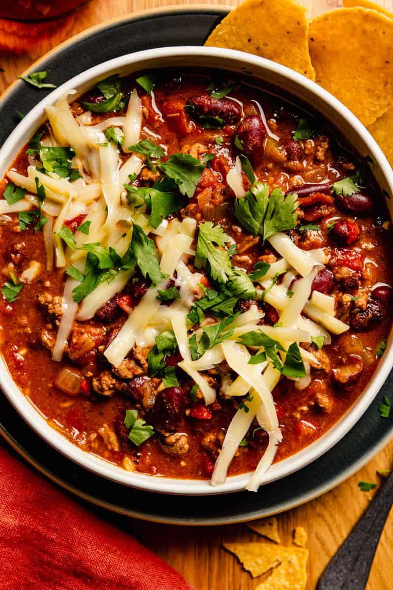 Quick chili in a shallow white bowl set on a blue plate. Chili topped with shredded cheese and cilantro.