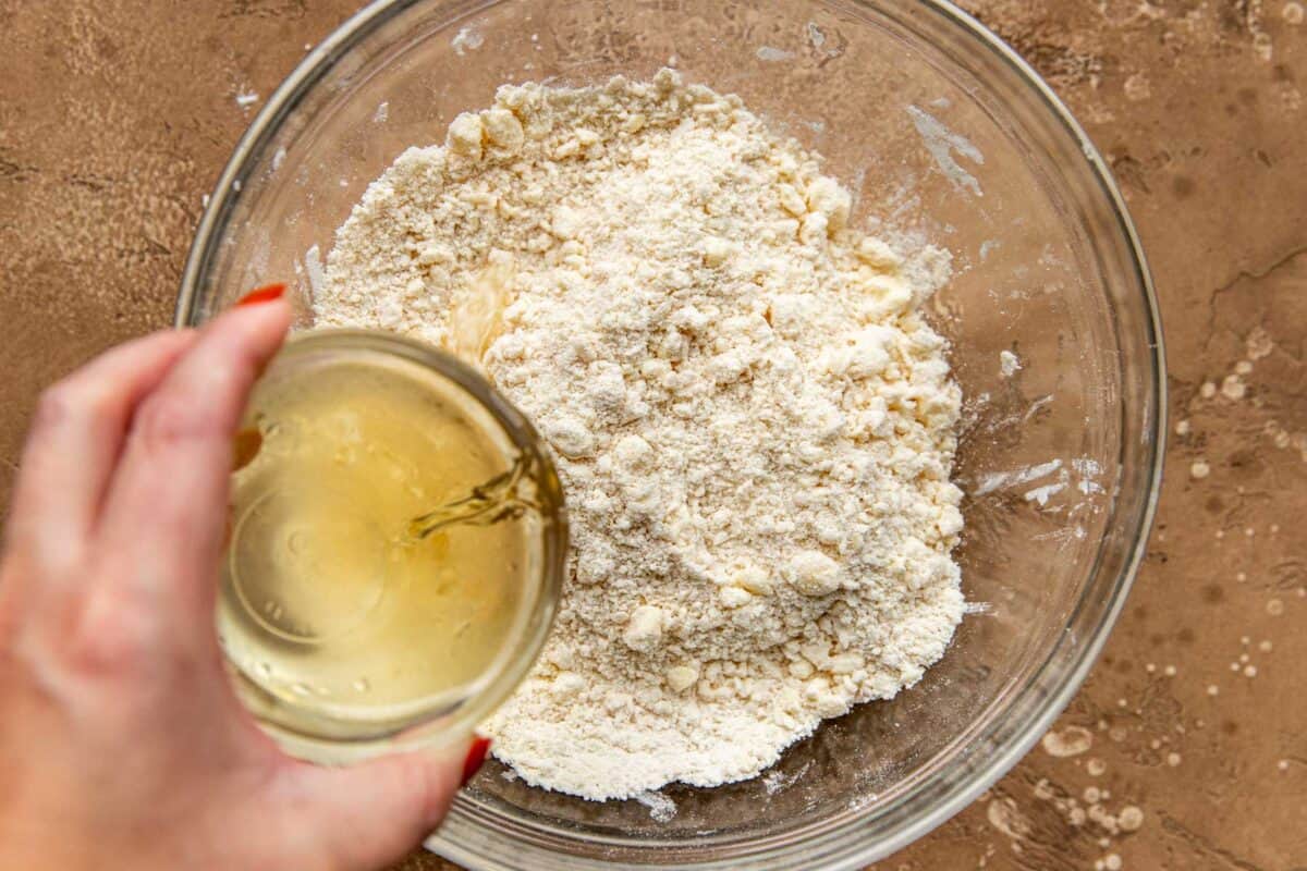 Flour and butter mixture in a glass bowl with bourbon and water being poured in.
