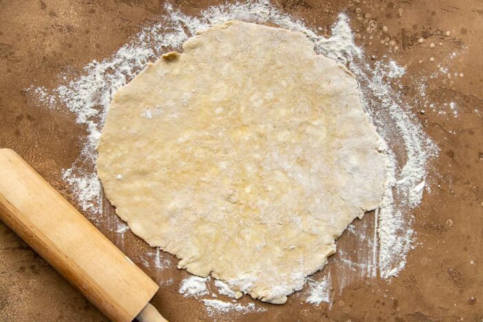 Pie crust rolled out on a work surface dusted with flour. A rolling pin set off to the side.