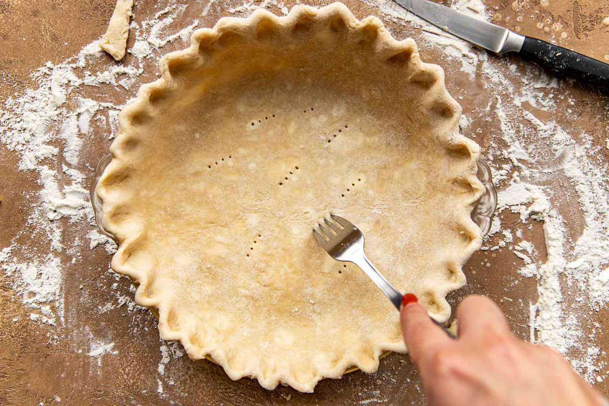 Unbaked pie crust in a pie plate getting docked with a fork.