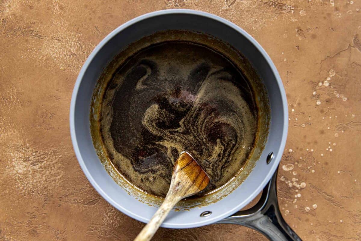 Maple syrup and brown sugar mixture in a saucepan with a wooden spoon set inside it.