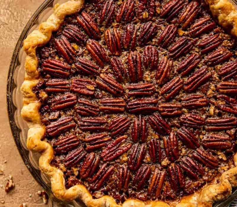 Bourbon Pecan Pie set on a brown background with a blue napkin and whipped cream set near by.