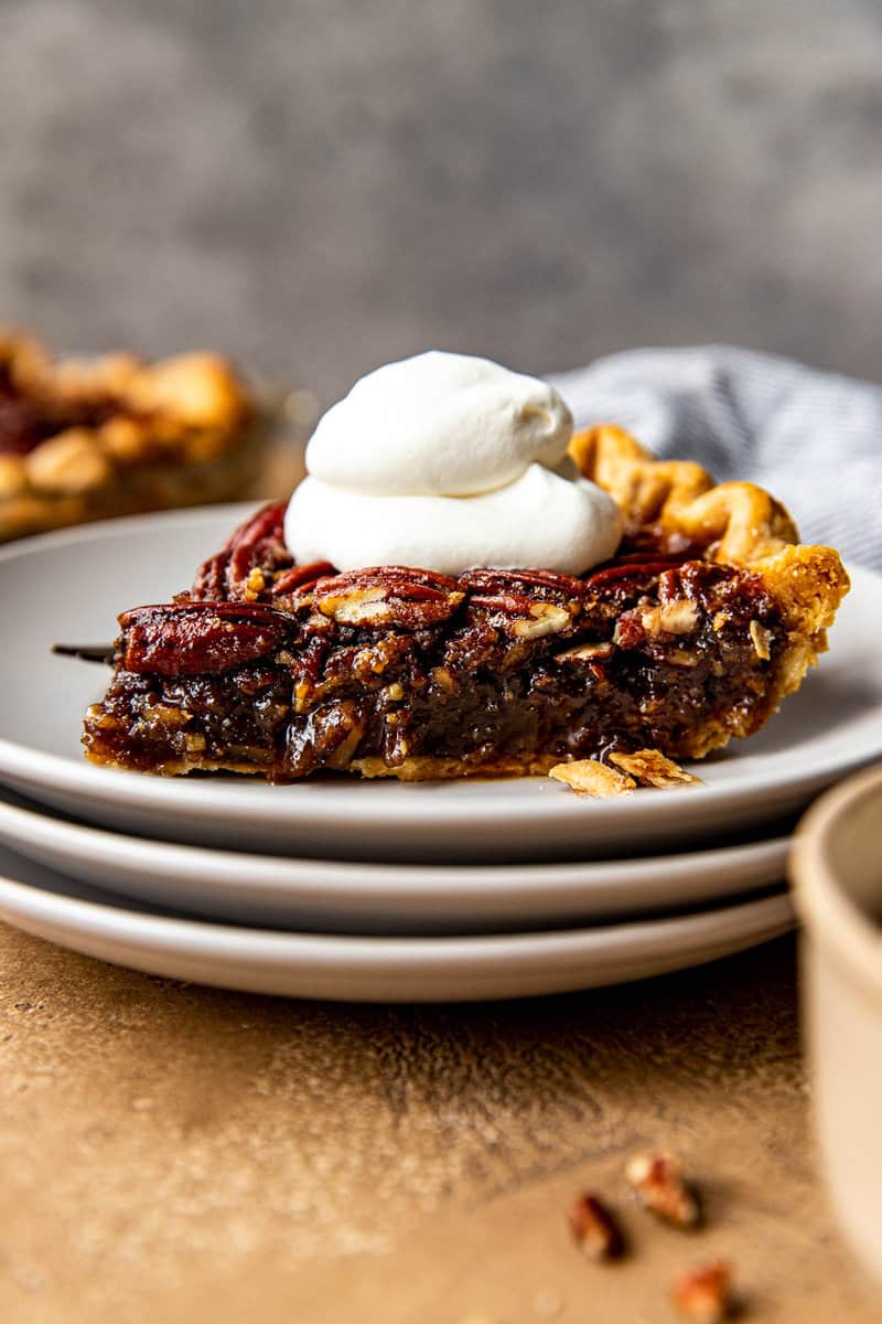 Slice of maple pecan pie on a white plate with whipped cream on top.