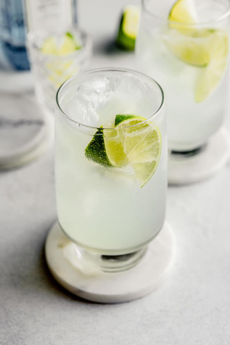 A simple Gin Rickey cocktail in a tall collins glass filled with ice and 2 lime wedges.