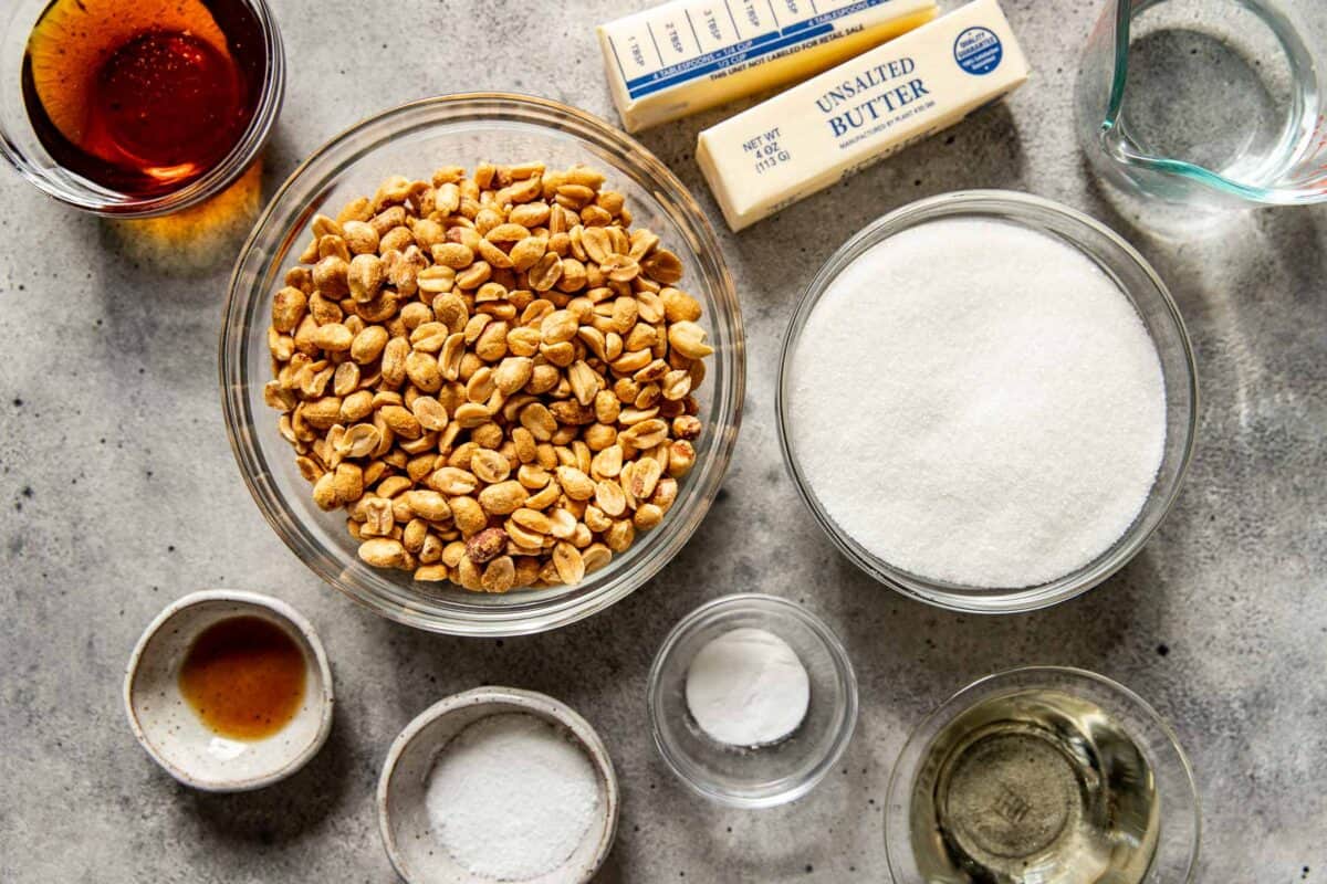 Ingredients for peanut brittle set out on a counter including roasted peanuts, sugar, corn syrup, butter, vanilla and salt set out on a counter.