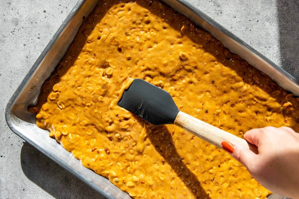 Old fashioned peanut brittle being spread into a quarter sheet pan with a rubber spatula.