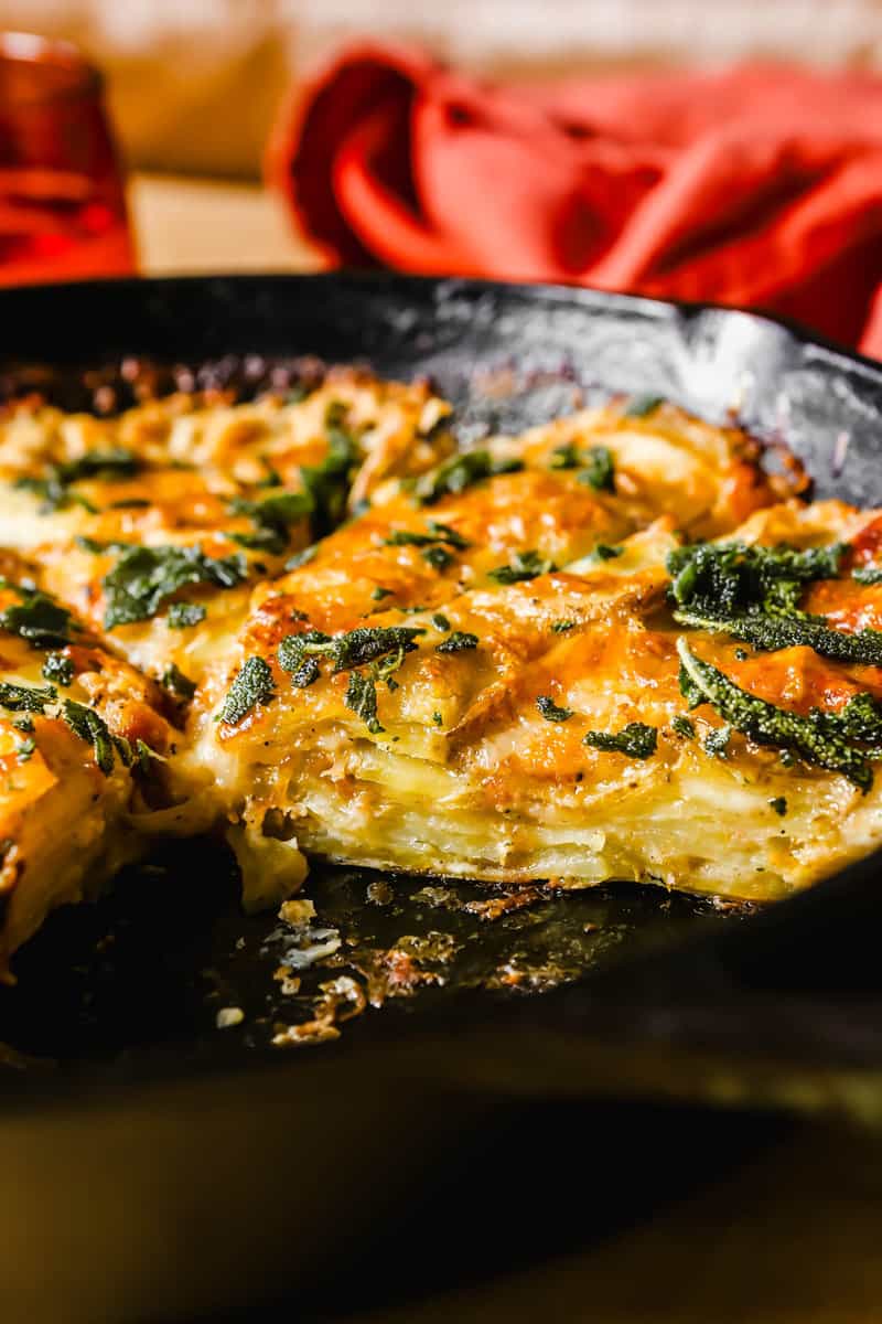 layers of potatoes and cheese in a cast-iron skillet with fried sage scattered over top.