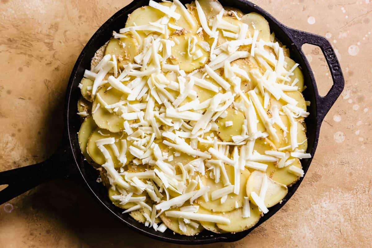 sliced potatoes and shredded cheesy layered in a cast-iron skillet for a potato au gratin