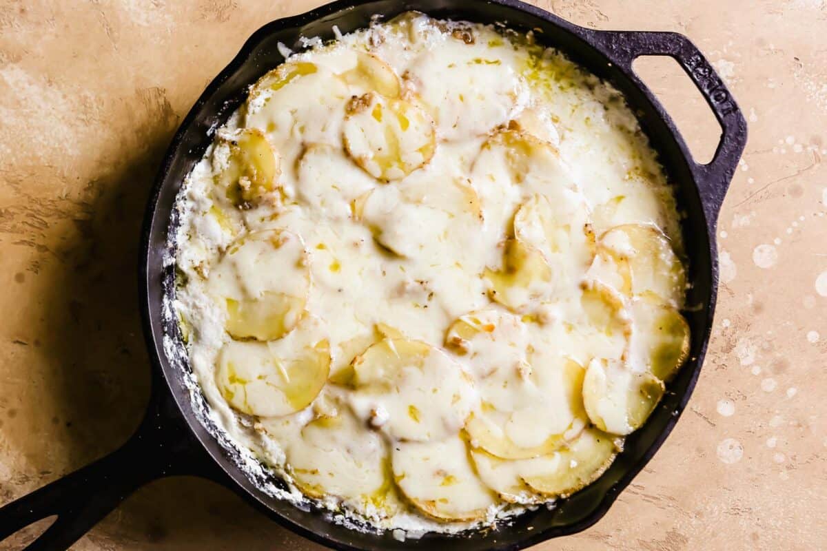cheese gruyere potato au gratin in a cast-iron skillet after foil is removed, not brown yet.