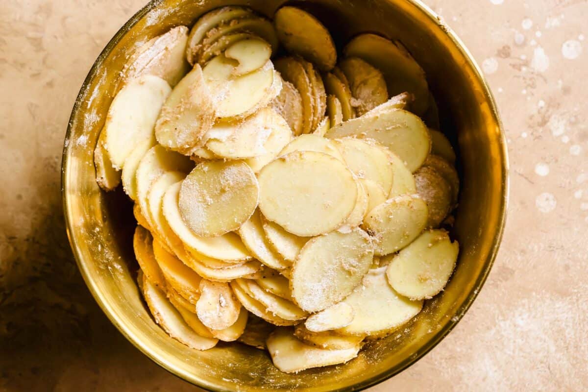 sliced potatoes in a brown bowl tossed with flour and spices.