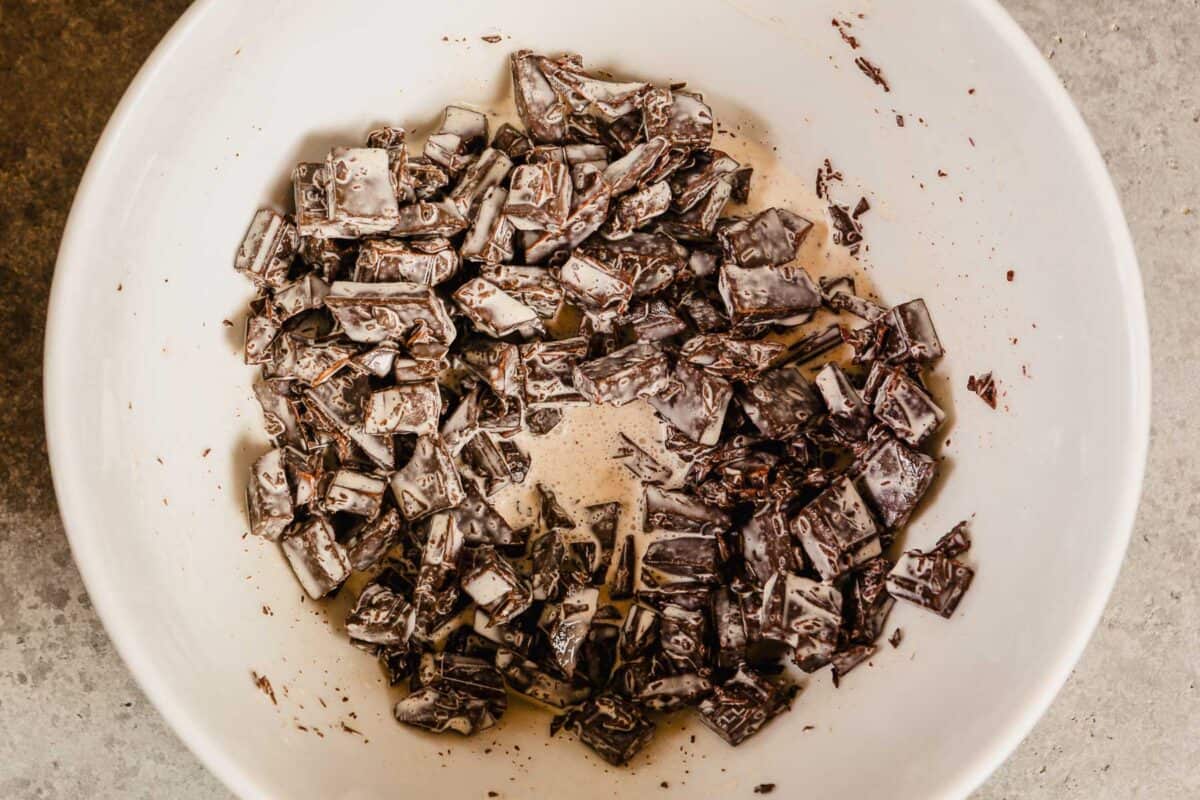 chunks of chocolate and heavy cream in a large white mixing bowl.