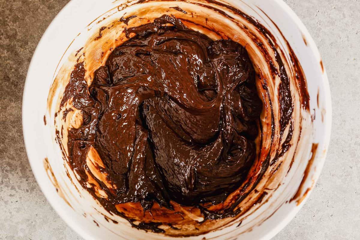 Melted chocolate ganache mixture in a large white mixing bowl.