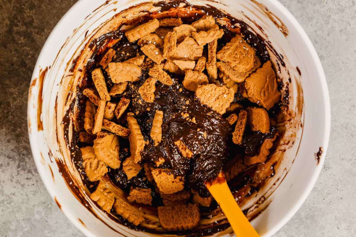 Chocolate ganache in a mixing bowl with broken biscoff cookies. 