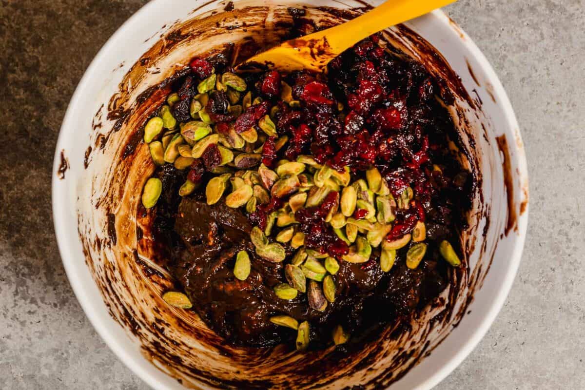Chocolate ganache mixture in a large white bowl with dried fruit and nuts.