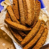 Gingerbread biscotti stacked on a metal platter lined with parchment paper.