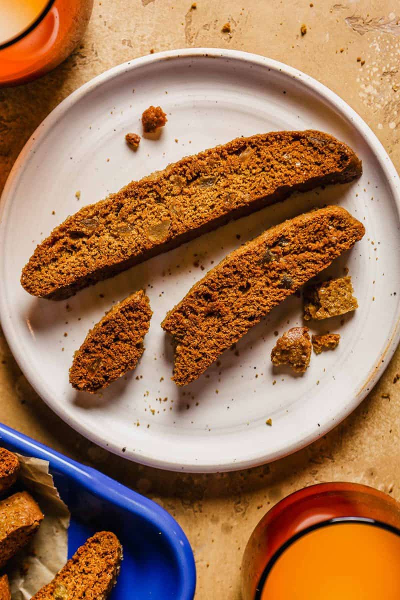 Crisp Gingerbread biscotti with chunks of candied ginger in it, on a small white dessert plate.