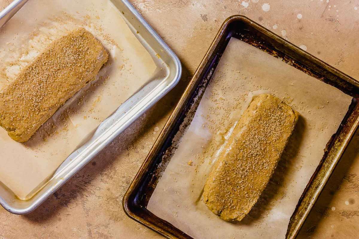 Unbaked gingerbread biscotti dough in two rectangles on parchment-lined baking sheets.