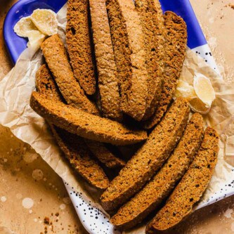 Gingerbread biscotti with chunks of candied ginger in it, stacked on a metal platter lined with parchment paper.