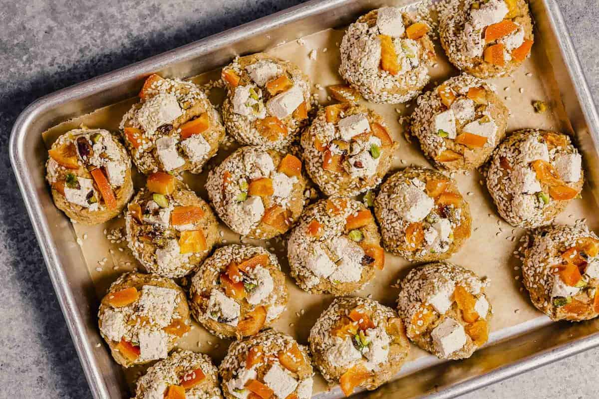 Cookie dough balls on a parchment-lined baking sheet with hunks of halva and candied orange stuck on top.