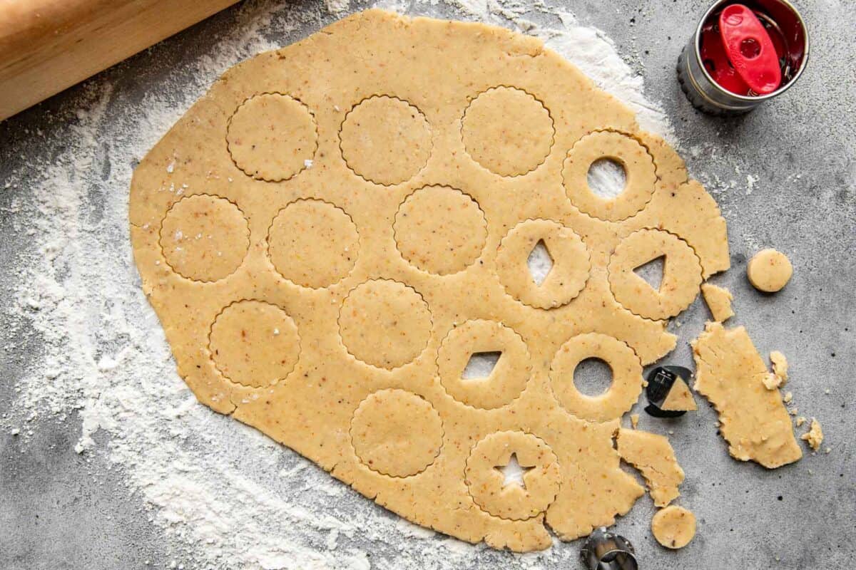 Linzer cookie dough rolled out and cut out on a floured work surface.